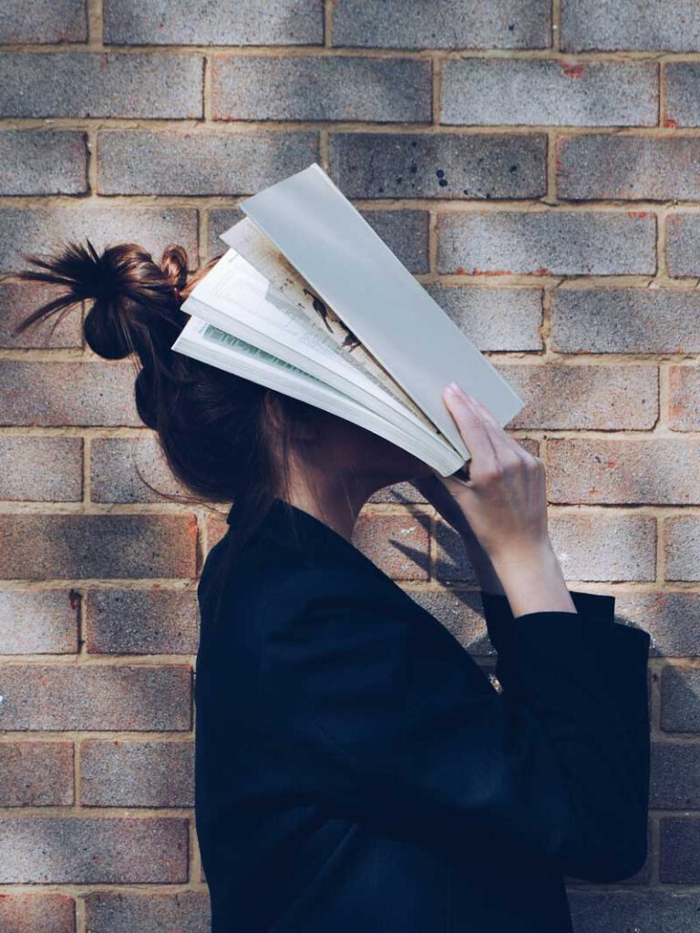 eine frau hält sich ein aufgeschlagenes buch vors Gesicht